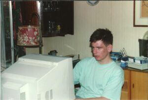 A young David Spink sitting in front of a largest CRT Monitor in the front room of a house.