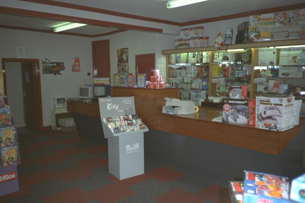 Interior of the ZigZak Computer shop with a long wooden counter and shelves behind with various stock on display.