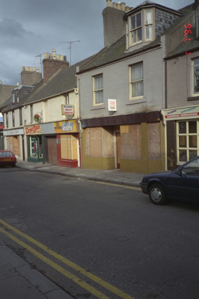 A view of a street with various shops with boarded up windows.