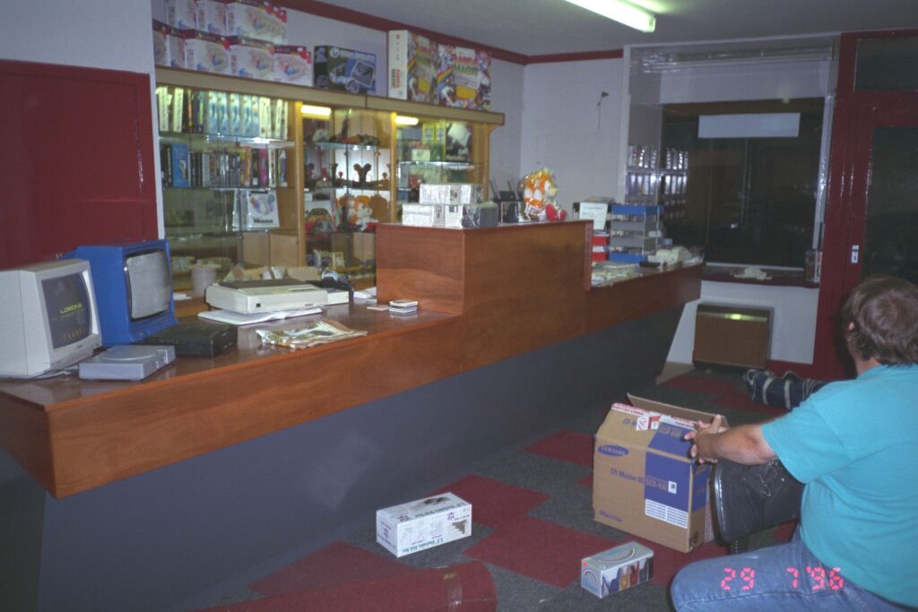 The interior of a shop being fitted out in 1996. A long wooden counter dominates the space with shelving behind.