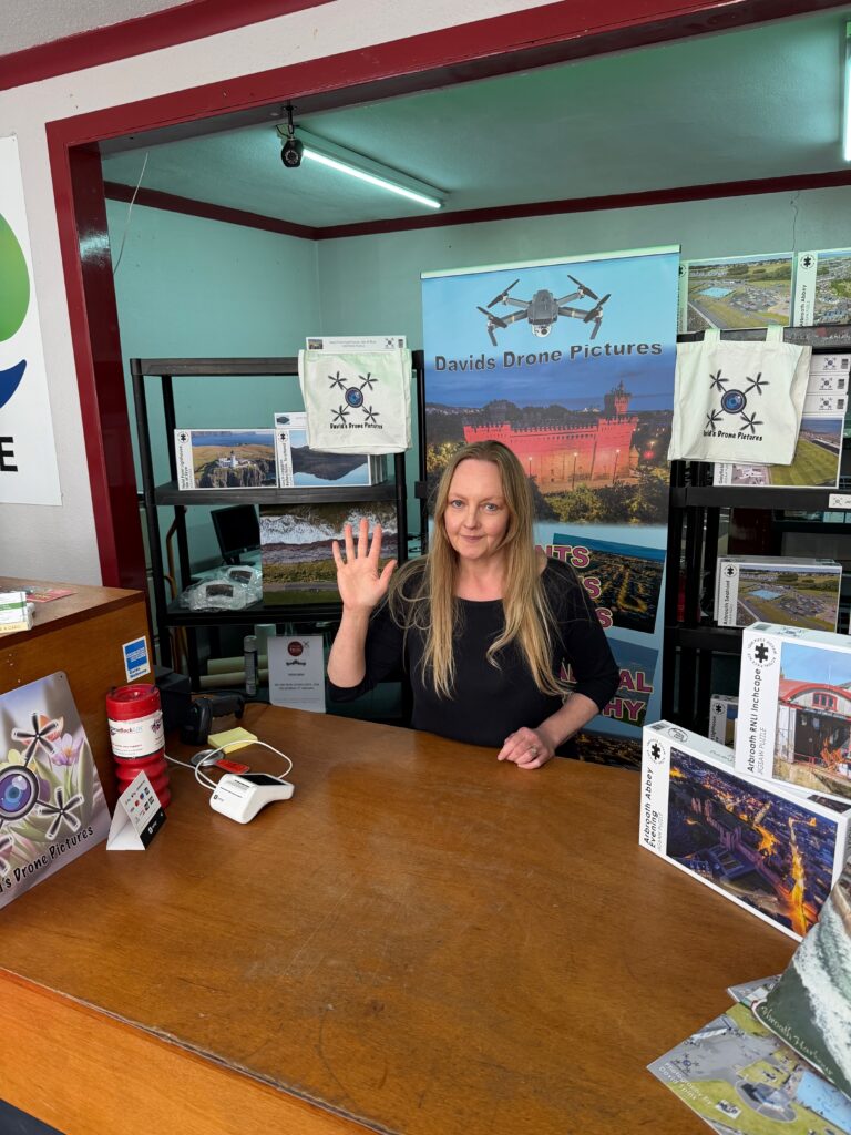 A women stands at a shop counter waving to the camera